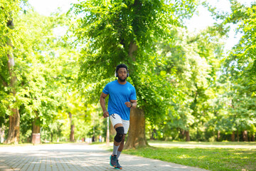 Young african american man jogging in park with knee brace during workout.
