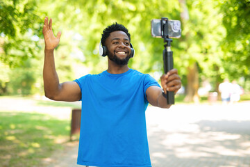 Smiling young african american man filming vlog with smartphone and gimbal outdoors.
