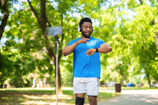Sporty african american man checking smartwatch while recording vlog in park.

