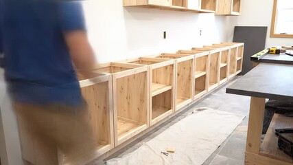 Professional cabinet maker assembling and installing a long row of custom wooden base cabinets during a new home construction project