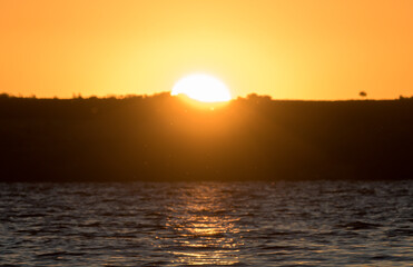Sunrise on the lake shore. The sun rises from behind the hills. 