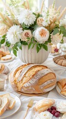 Round loaf of sourdough bread as a centerpiece on white tablecloth with flower arrangement, sliced bread, grapes, and decorative roses creating a beautiful table setting Round loaf