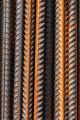 Detailed vertical macro photo of steel reinforcement bars featuring orange rust