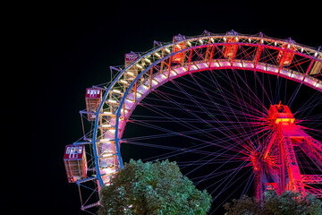 Illuminated Ferris Wheel with Vibrant Red and Yellow Lights in a Nighttime Urban Setting