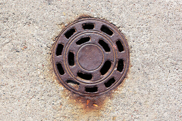 Rusty round sewer grate on concrete ground. Old circular manhole cover with corrosion stains. Urban...