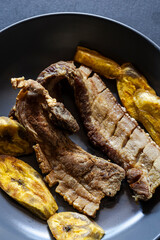 Crispy Fried Pork Belly with Fried Plantains on Dark Plate