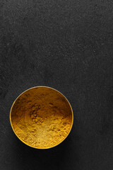 Turmeric powder in metal bowl on black slate background