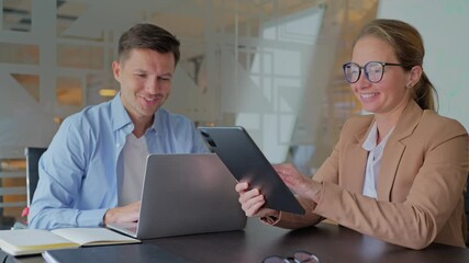 Colleagues people discuss strategy while using laptops and a tablet in an office.