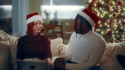 Pair of multiethnic friends or lovers discussing Christmas party at home. Caucasian woman and African American man chatting and using modern laptop, young spouses celebrating Xmas and New year