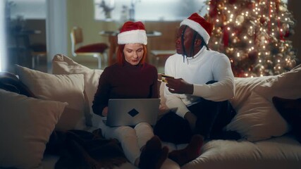 Cheerful customers of web-store ordering gifts online in Christmas holidays. Happy black man and his beloved caucasian lady shopping online and celebrating winter holidays, laughing multiethnic people
