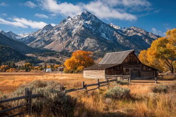 Old barn in a golden field with mountains and blue sky in the background. Perfect for travel, nature, or rural themed projects and designs.