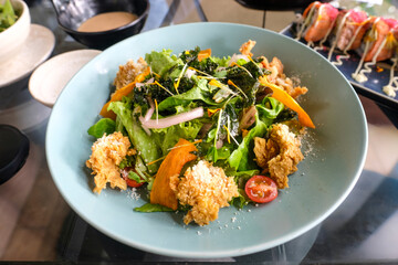 Fresh Japanese salad with crispy fried chicken, mixed vegetables, and colorful garnish served in a blue plate on restaurant table. Healthy Asian cuisine food photography with natural light