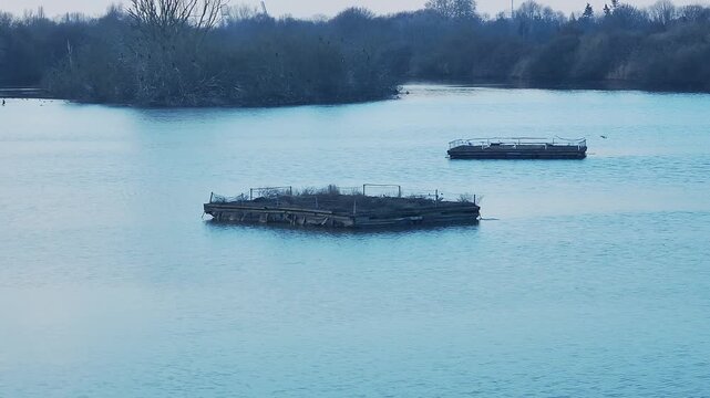 See im mit hellblauem Wasser und zwei schwimmenden Plattformen f&uuml;r Wasserv&ouml;gel.. Im Hintergrund eine Vogelinsel, Zu Beginn einzelne fliegende V&ouml;gel, in der zweiten H&auml;lfte zahlreiche fliegende V&ouml;gel.