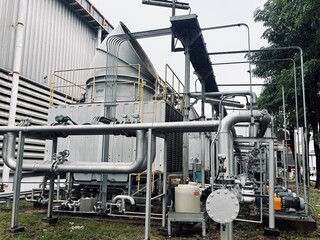 An industrial cooling tower and complex pipe system at an outdoor factory or power plant. The photo captures the scale and intricate design of the heavy machinery, contrasting with the natural element