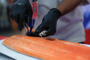The chef is preparing, handling, deboning or slicing fresh salmon. Close up hand of chef with salmon sashimi.
