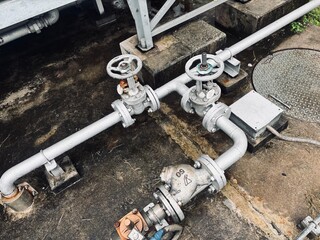 Industrial piping system with manual valves and flanges, set against a concrete background. This setup is typical for water, oil, or gas supply lines in a factory or refinery.
