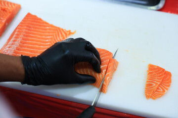 The chef is preparing, handling, deboning or slicing fresh salmon. Close up hand of chef with salmon sashimi.