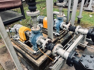 A pair of industrial water pumps with electric motors and connected pipelines, mounted on a concrete base outdoors. The photo highlights the mechanical components and the intricate connections 