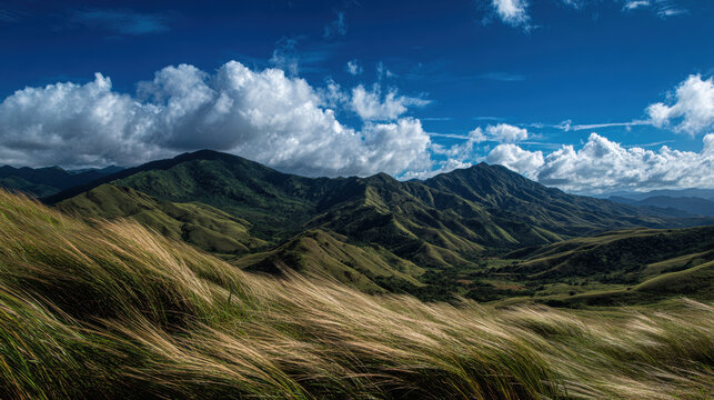 Lush green mountains under a bright blue sky filled with fluffy white clouds, rolling hills covered in grass swaying gently in the breeze, serene nature landscape.