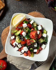Fresh vegetable salad with feta cheese and lemon served in a white bowl on a rustic wooden table