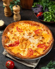 Freshly baked pizza with tomatoes and cheese served on a rustic table surrounded by greens and seasonings