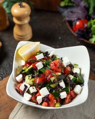 Fresh vegetable salad prepared with a mix of tomatoes, cucumbers, and feta cheese, served with a lemon wedge on a rustic wooden table