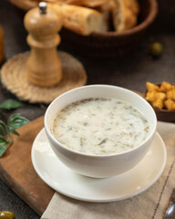 Creamy herb soup served in a white bowl with bread and snacks on a wooden table in a cozy setting