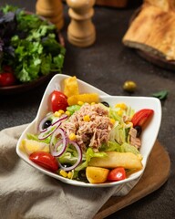 Fresh salad with tuna, vegetables, and fruits captured in a cozy kitchen setting with rustic decor and simple ingredients