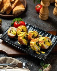 Deliciously plated gourmet chicken rolls drizzled with mustard on a black dish in a cozy dining...