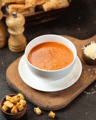 Savory tomato soup served in a white bowl with croutons and cheese on a wooden board