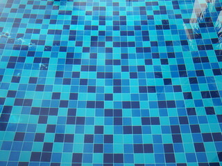 The pool is tiled with blue ceramic tiles. Blue water serface. Take a photo through the water in the pool and see the various shades of blue ceramic at the bottom. Reflection of trees in water
