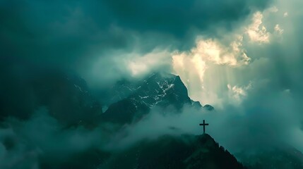 Fototapeta premium A lone religious cross stands atop a foggy mountain peak under dramatic, moody daylight.