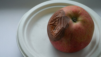 Close-up of a rotten apple with a wrinkled brown spot on a white plate.