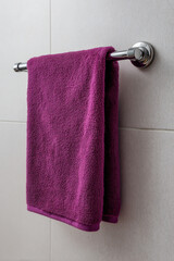 A purple terry towel hangs on a towel rail in the bathroom
