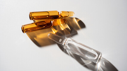 Different ampoules of serum in amber and clear glass on a bright surface during daylight
