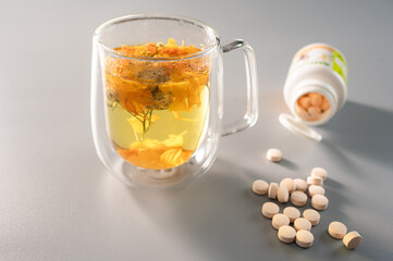 Health drink with herbal tea and supplement tablets on a gray background