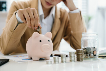 Stressed businessperson holding piggy bank with stacked coins and jar of money, symbolizing financial pressure, savings challenges, and economic stress.