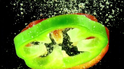 Multicolored Peppers. Slices of red, yellow and green peppers randomly fall in the water on a black background. Slow Motion - Powered by Adobe