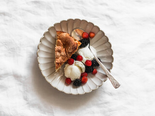 A piece of apple pie with ice cream and fresh berries on a light background, top view