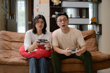 Obraz premium A couple sits close on a brown sofa, smiling while playing video games with handheld controllers