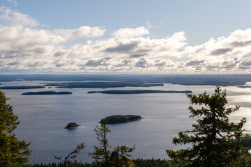 Witness the stunning panorama of Koli National Park in Finland. Serene lakes glisten under the sky, surrounded by dense forests and distant islands, creating a peaceful natural landscape.