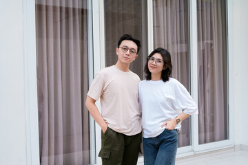 A relaxed couple stands close smiling, with arms around each other outside a modern glass window