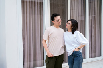 A relaxed couple stands close smiling, with arms around each other outside a modern glass window