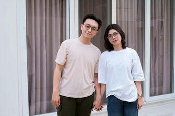 A relaxed couple stands close smiling, with arms around each other outside a modern glass window