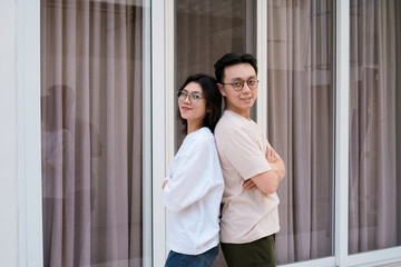 A relaxed couple stands close smiling, with arms around each other outside a modern glass window