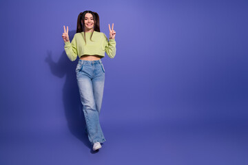 Happy young female in casual crop top and jeans making peace signs with hands against vibrant purple background