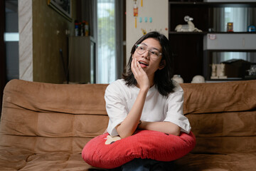 Obraz premium A relaxed woman in a white shirt sits on a brown couch, hugging a red pillow in a cozy living room