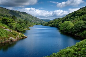 Fototapeta premium Still deepblue water flows through a valley between verdant rocky mountains under a cloudy sky