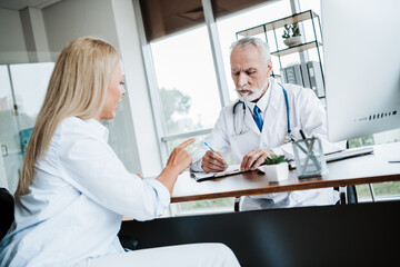 Middle-aged doctor discussing medical inquiries with a patient in a modern clinic office during a...
