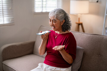 Older Asian woman voice calls using smartphone home living room modern technology senior digital communication connection lifestyle independent comfort